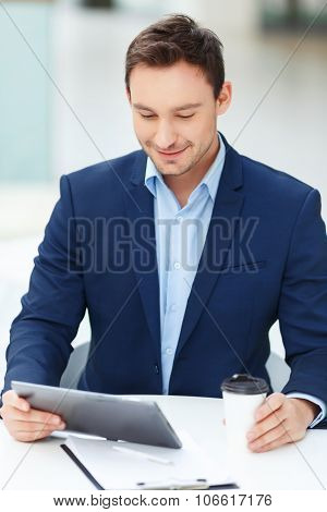 Young gentleman with tablet and papercup of coffee.