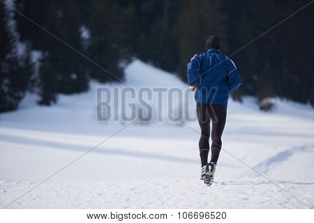 young  man jogging on snow in forest, bautiful sunny winter day. handsome sporty ahtlete man running