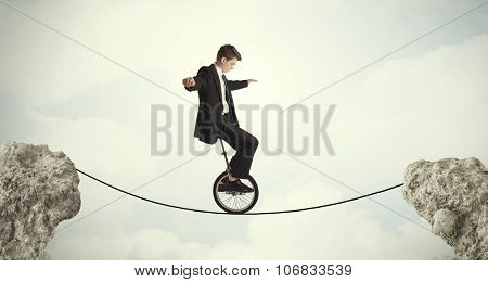 Brave business man riding an mono cycle between cliffs concept