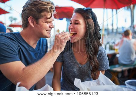 playful boyfriend feeding his girlfriend a french frie
