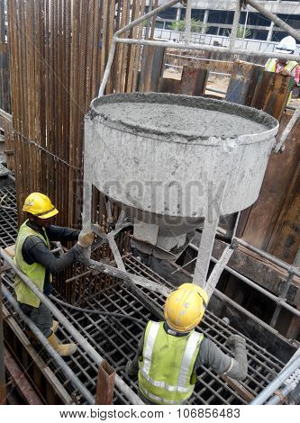 A group of construction workers pouring concrete slurry into pile cap formwork