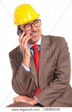 side view of a smiling old construcion engineer talking on the phone and looks away from the camera