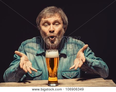 The spellbound man in denim shirt with glass of beer
