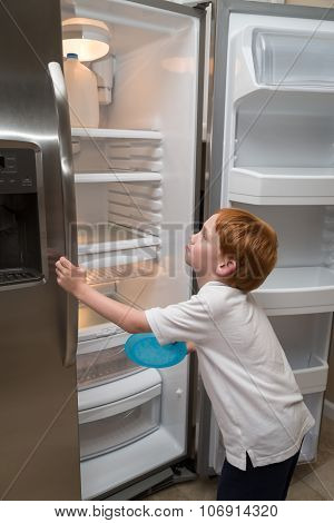 Hungry little boy looking into empty fridge
