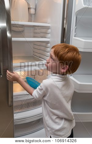 Hungry little boy looking into empty fridge