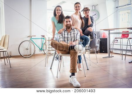 Portrait of four co-workers smiling and looking at camera while wearing cool casual clothes, during work in the shared office space of a modern hub for freelancers and young entrepreneurs