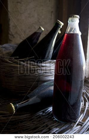 old and dusty botlles of aged red wine in a wicker basket illumined through a window
