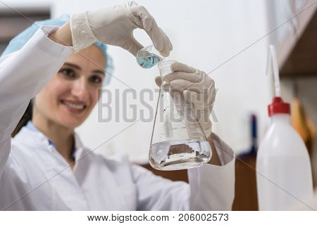 Low-angle view of the hands of a successful chemist smiling while mixing two liquid chemical substances during an innovative experiment in an industrial lab