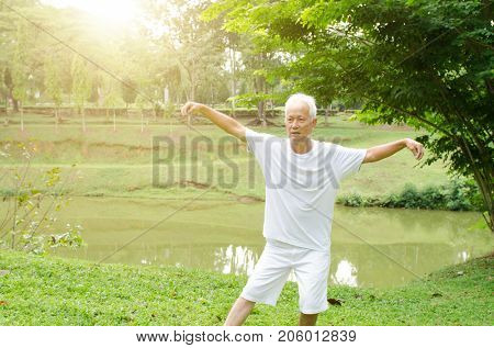 Portrait of healthy white hair Asian senior man practicing wushu at outdoor park in morning.