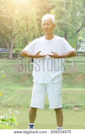Portrait of healthy grey hair Asian old man practice taichi at outdoor park in morning.