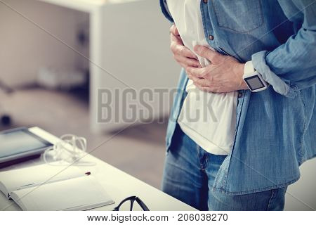 Food poisoning. Unhappy nice adult man holding his stomach and feeling pain while having food poisoning