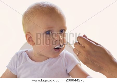 Mother feedding her one year blonde blue-eyed toddler with a yogurt.