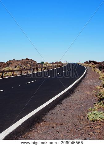 long winding curve in an empty road with mountains in the background arid summer landscape and blue sky