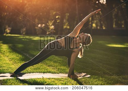 Beautiful sporty fit yogini woman practices yoga asana Parivritta Parshvakonasana - Revolving side angle posture in the park at sunset