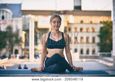 Beautiful sporty fit yogini woman practices yoga asana Cow Face pose gomukhasana in the city