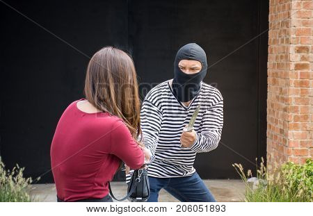 Male robber robbing a handbag threatening with knife to scared Asian woman,criminal concept