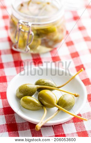Pickled caper berries in bowl on checkered tablecloth.