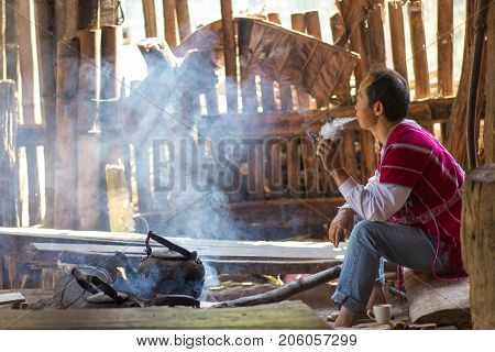 MAE KLANG LUANG, THAILAND, FEBRUARY 2, 2017 : A Karen tribe man is sitting and smoking a cigarette, waiting for the tea water to boil in the village of Mae Klang luang near Chiang Mai, Thailand