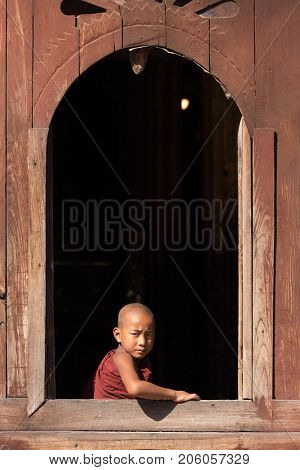 NYAUNG SHWE, MYANMAR, JANUARY 27, 2015 : A young novice buddhist monk is looking at the window of the Shwe Yaunghwe Kyaung monastery in Nyaung Shwe, Myanmar (Burma).