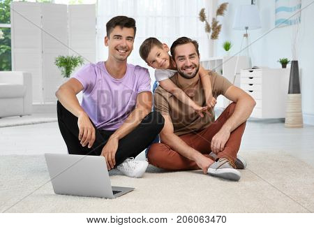Male gay couple with foster son sitting on floor at home. Adoption concept
