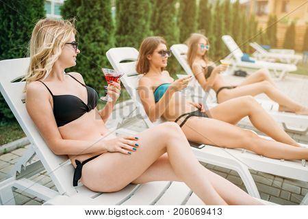 Three slim girls relax on deck chairs outdoors