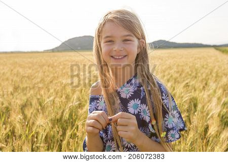 An Adorable little girl playing in the wheat field on a warm summer day
