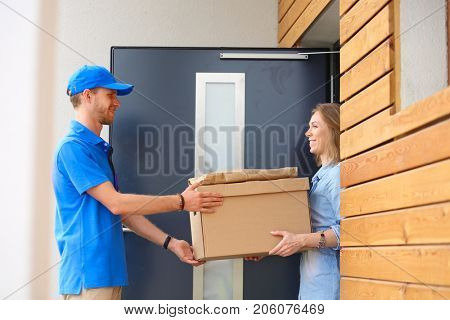 Smiling delivery man in blue uniform delivering parcel box to recipient - courier service concept. Smiling delivery man in blue uniform