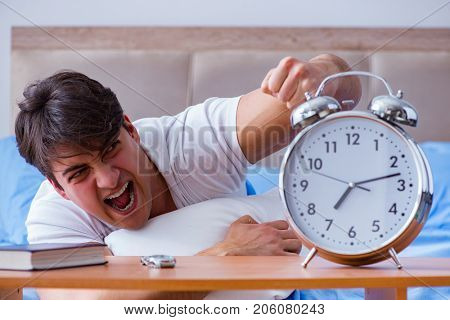 Man in bed frustrated suffering from insomnia with an alarm cloc