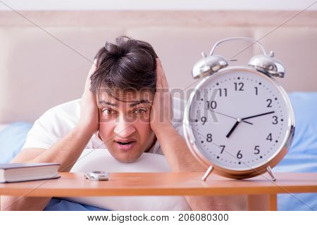 Man in bed frustrated suffering from insomnia with an alarm cloc