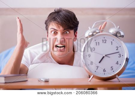 Man in bed frustrated suffering from insomnia with an alarm cloc