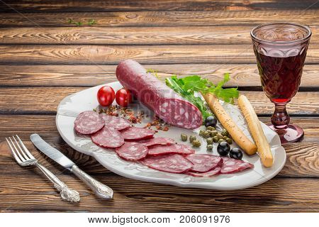 Sausage with red wine olives capers tomates and harbs over wooden background