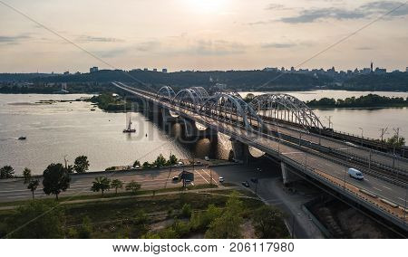 Aerial top view of automobile and railroad Darnitsky bridge across Dnieper river from above, Kiev (Kyiv) city sunset skyline, Ukraine