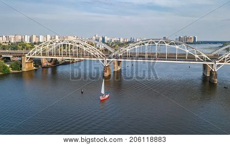 Aerial top view of Darnitsky bridge, yachts and boats sailing in Dnieper river from above, Kiev (Kyiv) city skyline, Ukraine