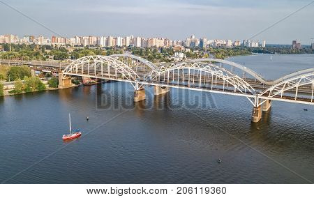 Aerial top view of Darnitsky bridge, yachts and boats sailing in Dnieper river from above, Kiev (Kyiv) city skyline, Ukraine