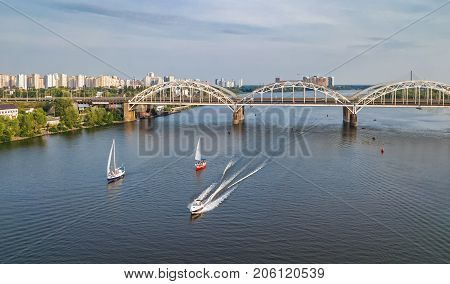 Aerial top view of Darnitsky bridge, yachts and boats sailing in Dnieper river from above, Kiev (Kyiv) city skyline, Ukraine