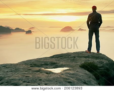 Man stands alone on the peak of rock. Hiker watching to autumn Sun at horizon . Beautiful moment the miracle of nature. Colorful mist in valley. Man hike. Person silhouette stand