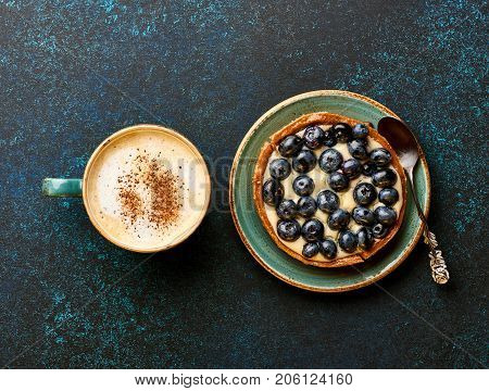 Blueberry tart with cup of coffee on blue stone background.