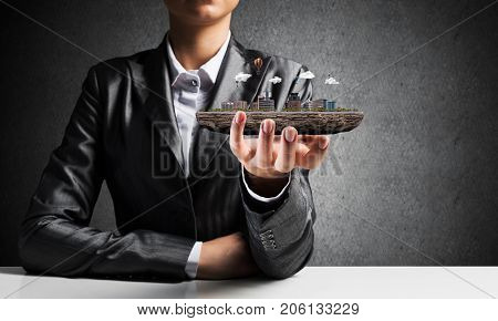 Cropped image of businessman in suit presenting in his hand modern city block with gray wall on background. 3D rendering.