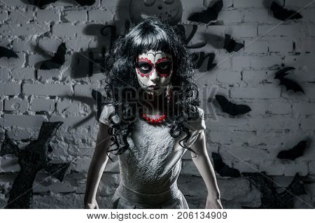 Little santa muerte girl with black curly hair and scary maleup is looking straight forward