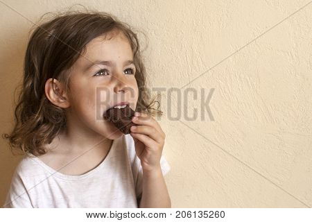 The girl enjoys a bite of a piece of milk chocolate