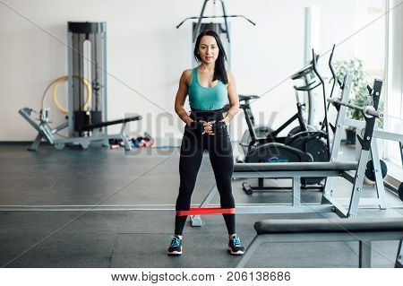 cute fit girl performs modern leg exercises with elastic rubber