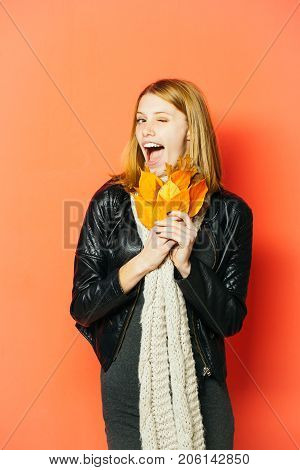 Season and autumn holiday. Girl with orange leaves on orange background. Woman with autumn leaves in leather jacket. Beauty and fashion. happy model with stylish hair in scarf.