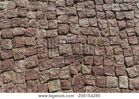 Square lined with cobblestone or stone pavement walkway or road. The surface of rough stones and rough. Stones brown. Seams of sand. The cobbles have a mottled pattern and texture.