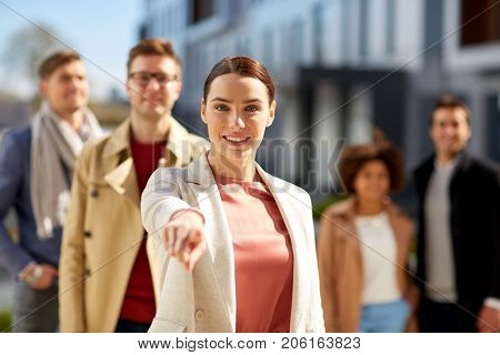 business, choice and corporate concept - happy smiling woman pointing finger at you with international group of people on city street