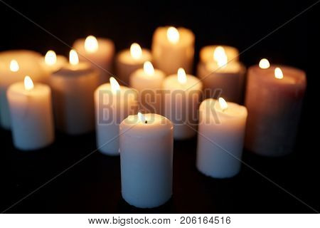 mourning and commemoration concept - candles burning in darkness over black background