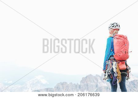 Female mountaineer with trad climbing rack including backpack, helmet, chalk bag, harness with spring-loaded cams, nuts, quickdraws, slings and carabiners enjoying view to valley, copy space