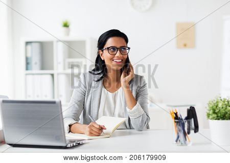 business, technology, communication and people concept - happy smiling businesswoman or secretary with notebook calling on smartphone at office