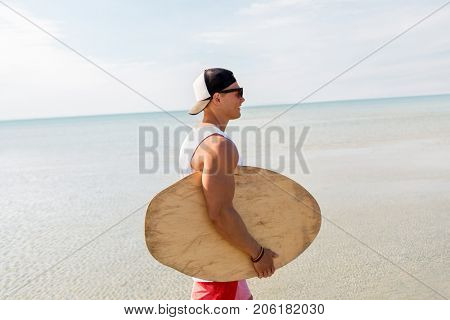 skimboarding, water sport and people concept - happy smiling young man with skimboard on summer beach