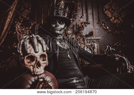 Halloween. A man with a skull makeup dressed in a tail-coat and a top-hat is in the old castle. Baron Saturday. Baron Samedi. Dia de los muertos. Day of The Dead. Old vintage interior.