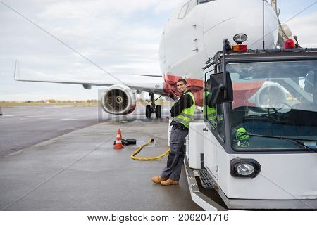 Worker Leaning On Towing Truck With Airplane In Background